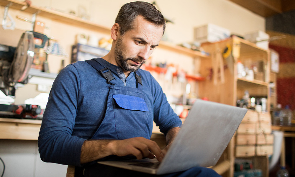 Comerciante con una laptop, de fondo se ve su pequeño negocio